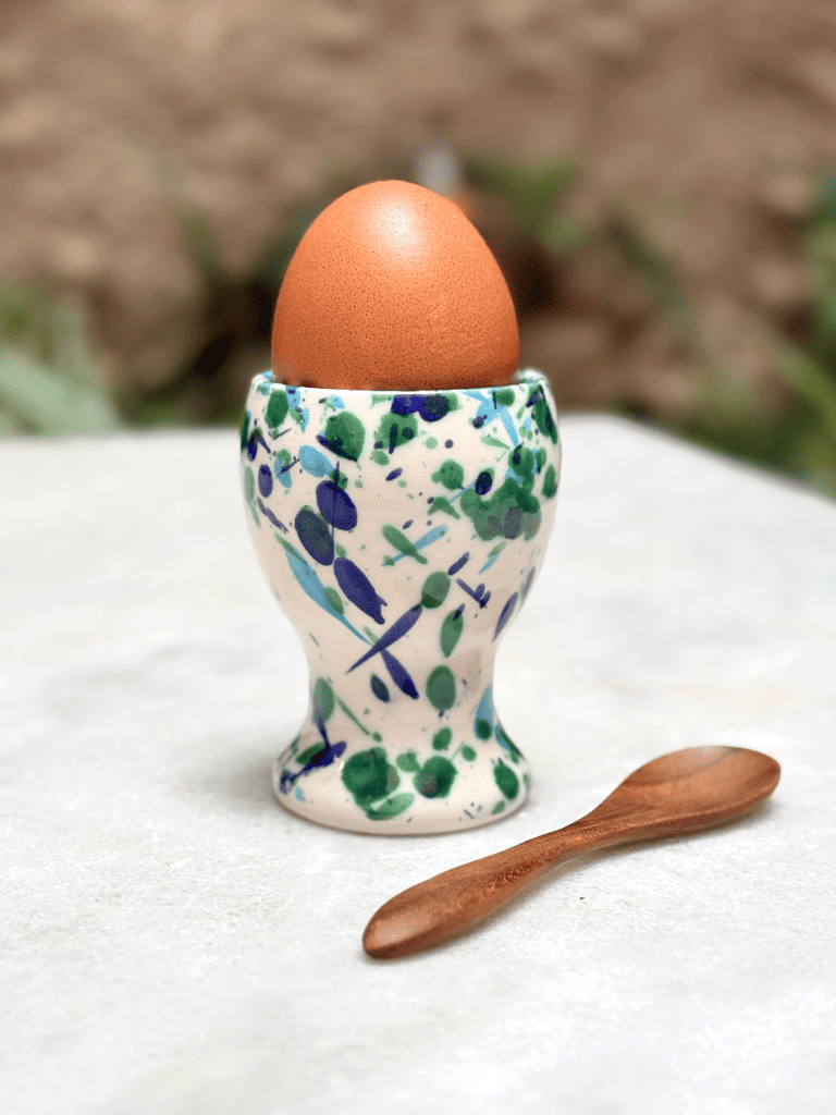 Coquetier artisanal en céramique contenant un œuf à la coque, décoré de taches bleu et vert