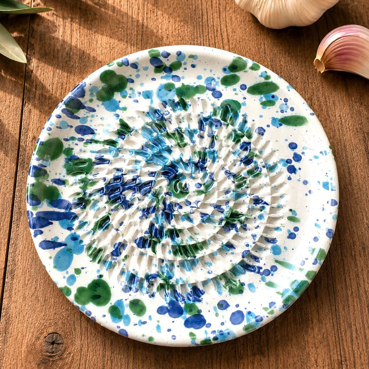 Petite coupelle poterie avec fond gratte ail et gingembre, avec taches de couleurs bleues vertes sur table en bois