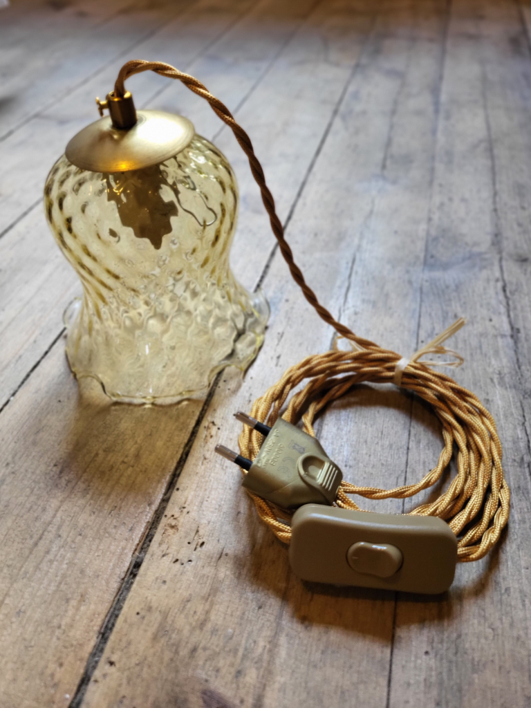 baladeuse ambre avec un câble doré posée sur un sol en bois