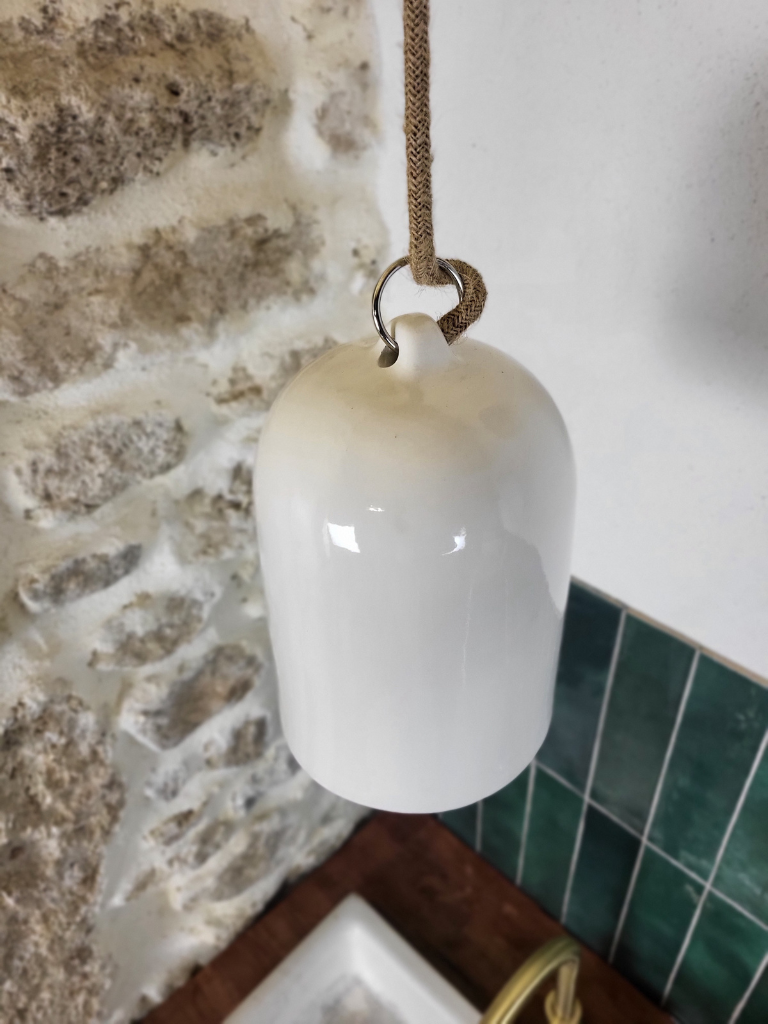 Suspension en céramique blanche suspendue à l'angle au-dessus d’un évier, près d'un mur carrelé vert et d'un mur en pierre fonctionnel et décoratif dans une cuisine au style naturel