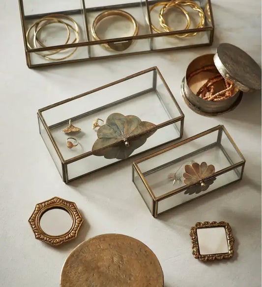 Boîte en verre vintage posée sur une table avec des bijoux, détail floral en métal