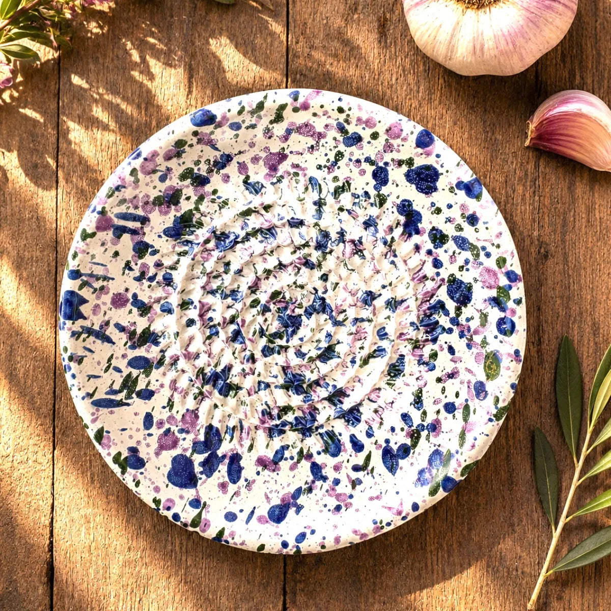 Assiette en céramique, gratte ail et légumes, taches bleues et violettes accessoire cuisine artisanale en céramique sur table en bois