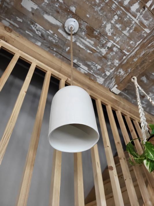 Vue en contre-plongée d’une suspension en céramique blanche avec une corde, à coté d'un escalier en bois clair et d'une plante