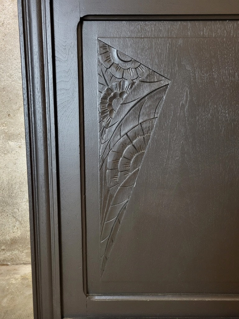 Gros plan sur les sculptures florales sculptées dans le bois massif du buffet, mises en valeur par une peinture noire élégante.