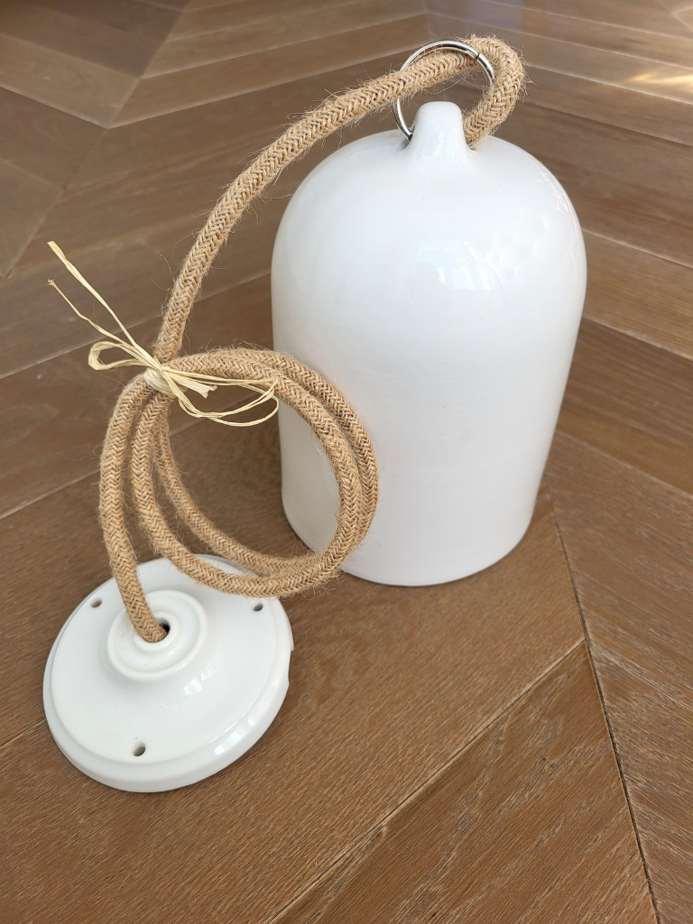 Suspension en céramique blanche positionnée sur un sol en bois, lumière douce et ambiance chaleureuse dans une pièce épurée