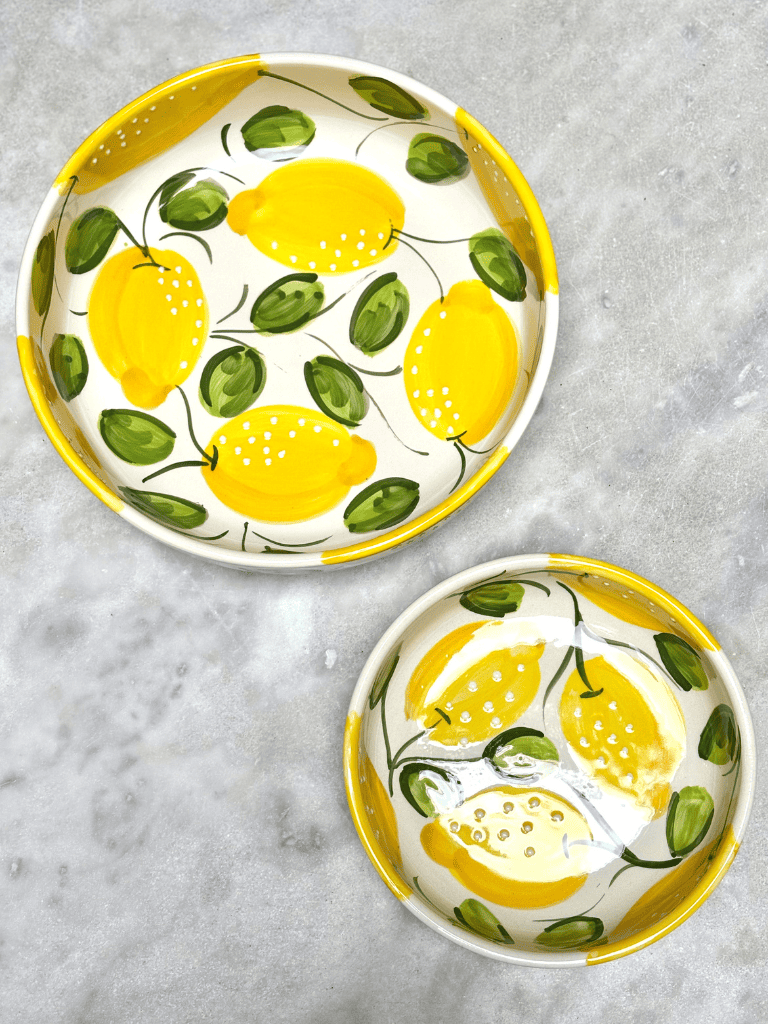 Plusieurs plats ronds à bord en terre vernissée décorés de citrons, présentés sur une table de repas, ambiance méditerranéenne