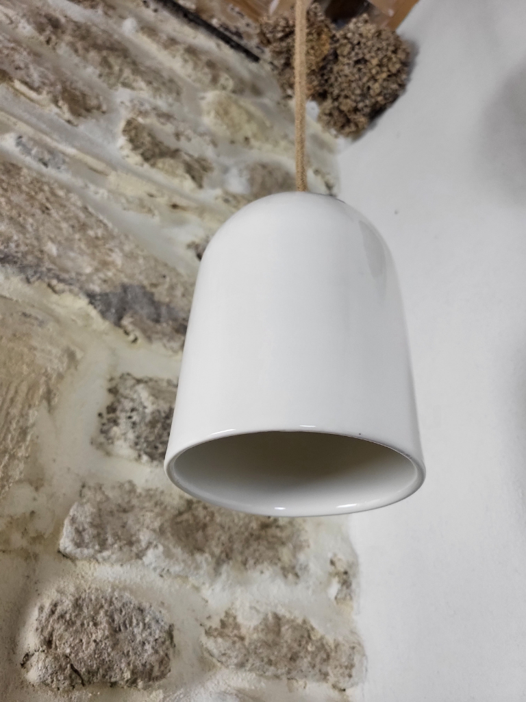 Suspension en céramique blanche installée près d’un mur en pierre dans l'angle de la pièce, éclairage vertical élégant et contemporain

