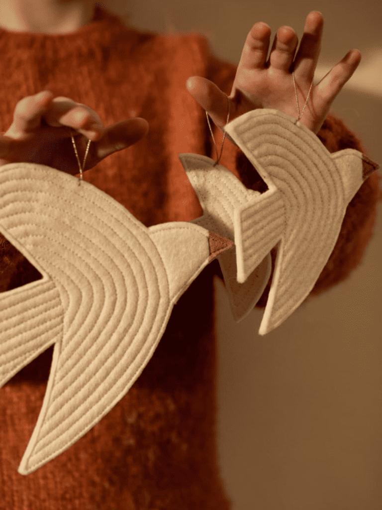 Suspensions oiseau Muskhane en feutrine beige suspendues sur les main d'un enfant