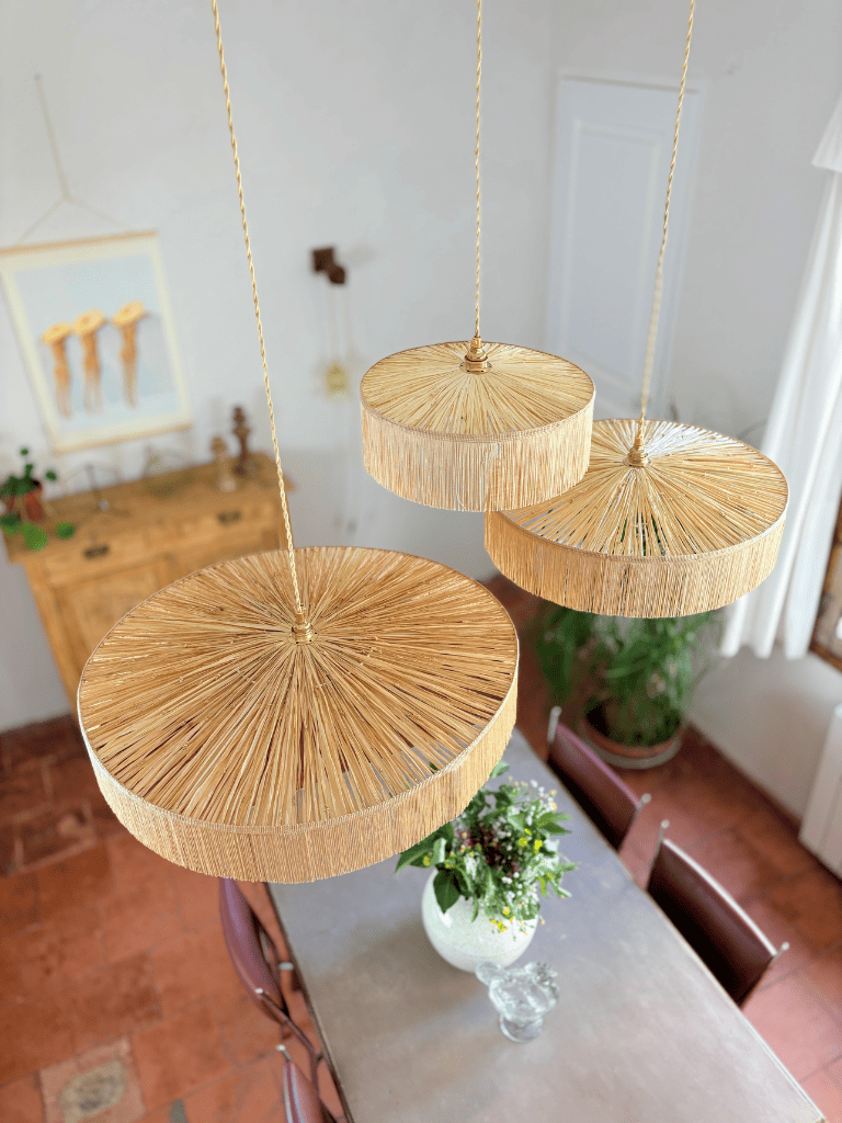 Trois abat-jours en raphia tissé main avec franges, vue du dessus sur fond sombre, ambiance bohème naturelle et chic.
