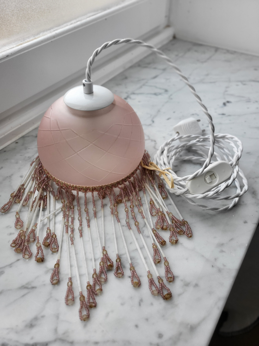 suspension perle rose placé proche d'une fenêtre sur un fond en marbre