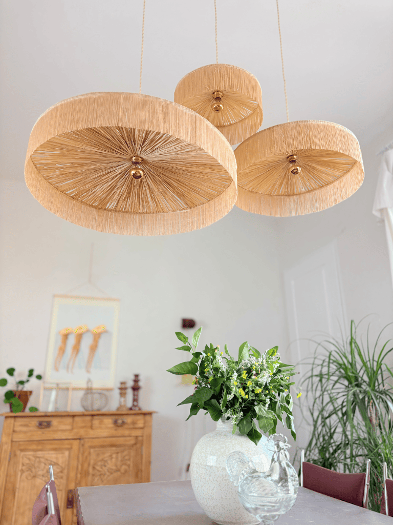 Trois abat-jours en raphia tissé main avec franges, vue du dessous sur fond sombre, ambiance bohème naturelle et chic.